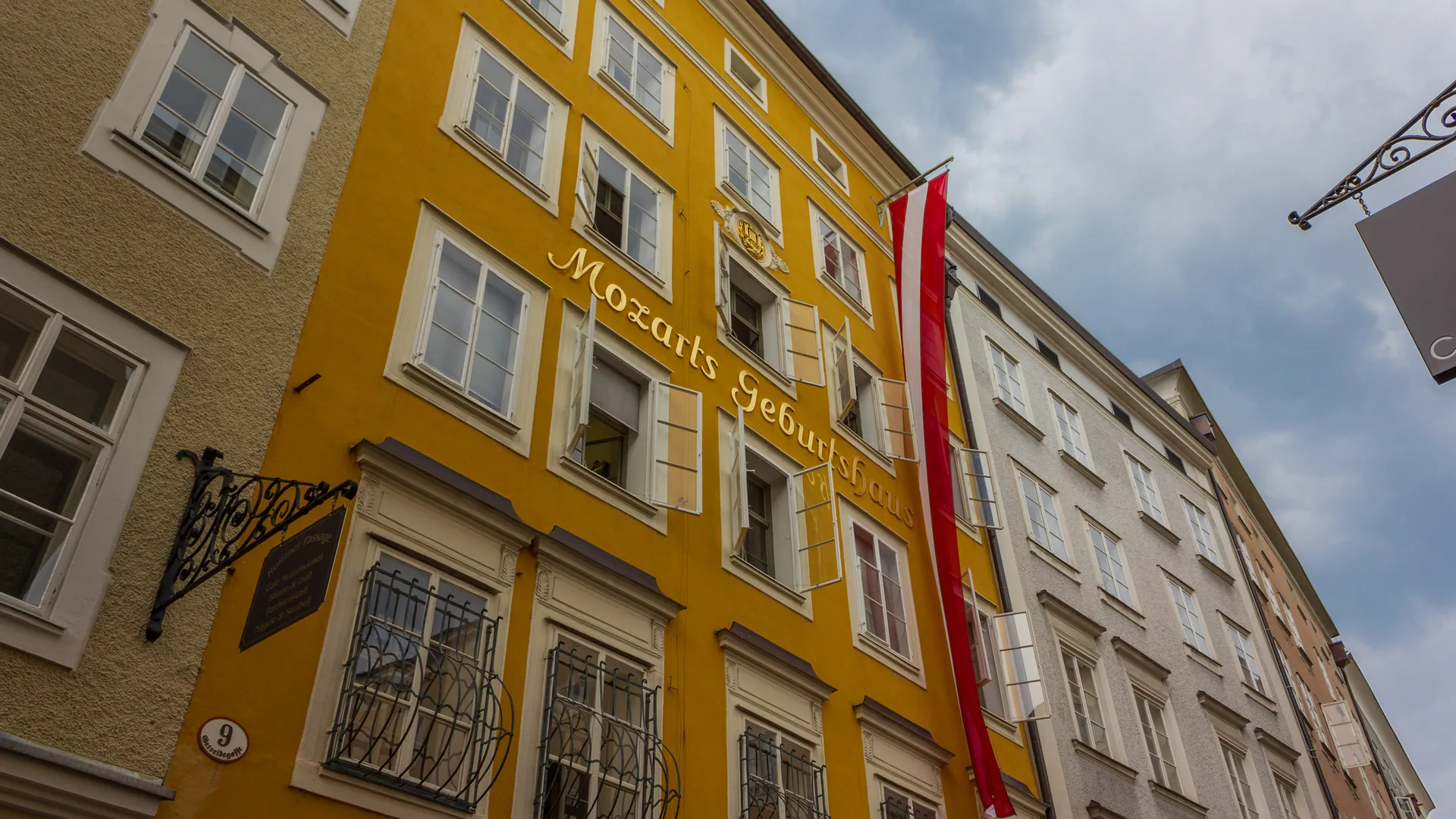 The bright-yellow Getreidegasse 9 townhouse facade in Salzburg lettered “Mozarts Geburtshaus,” with an Austrian flag hanging from it.